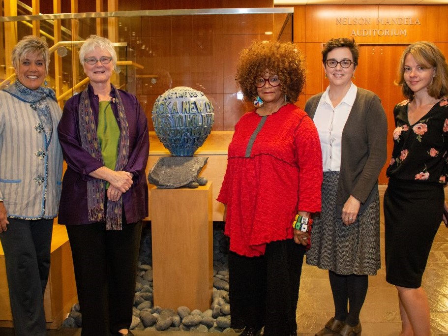 Five women posing next to a statue of a globe