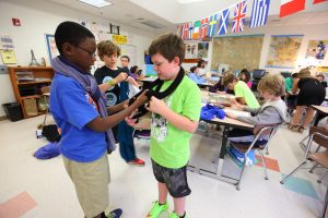 Two students help each other put on scarves in a classroom
