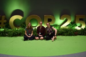 Three women kneeling in from of COP25 display.