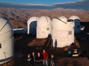 Group of five stand in front of large telescopes.