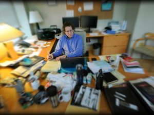 Adam Versényi sits at desk with a blurred effect around him.