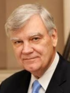 Headshot of Atwood. He has gray hair and is wearing a black blazer over a white collared shirt and a Carolina blue tie.