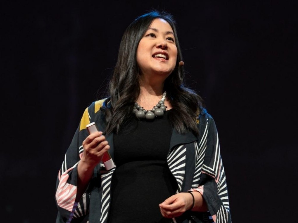 Hsu lecturing at a Ted Talk. Holding a remote and wearing a microphone.