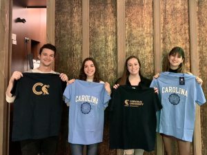 Four students each holding up t-shirts. Half of the shirts have the UNC logo on them, and the other half have the Cornivus University logo on them.