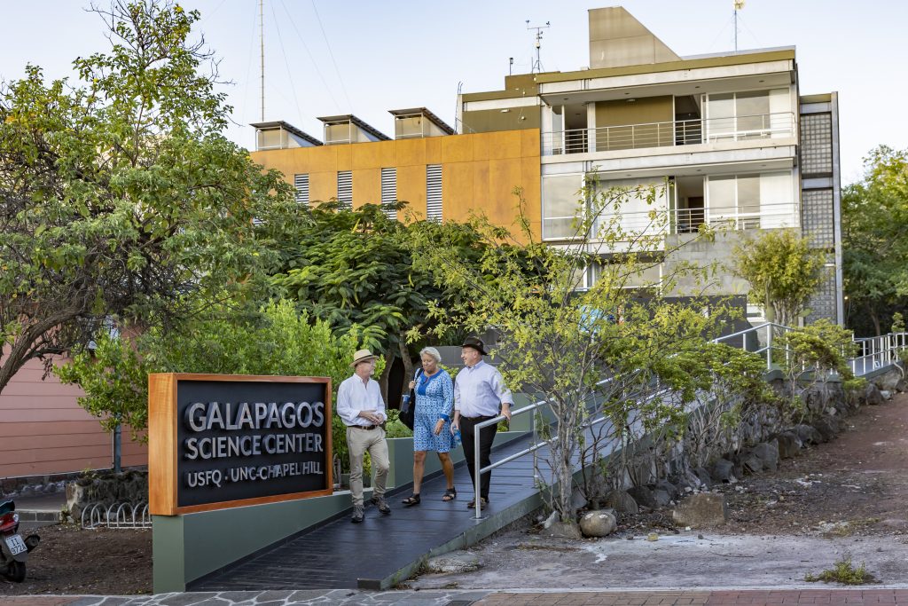 Three people walk down a ramp in front of a building. There is a sign in front of the building that says "Galapagos Science Center USFQ UNC-Chapel Hill"